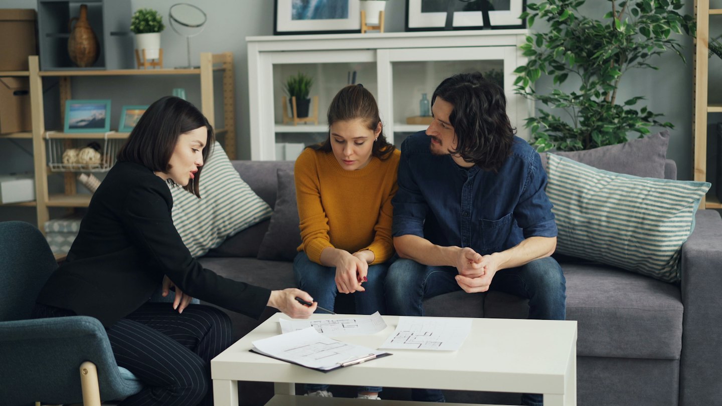 Real estate agent points to floor plans with a young couple.